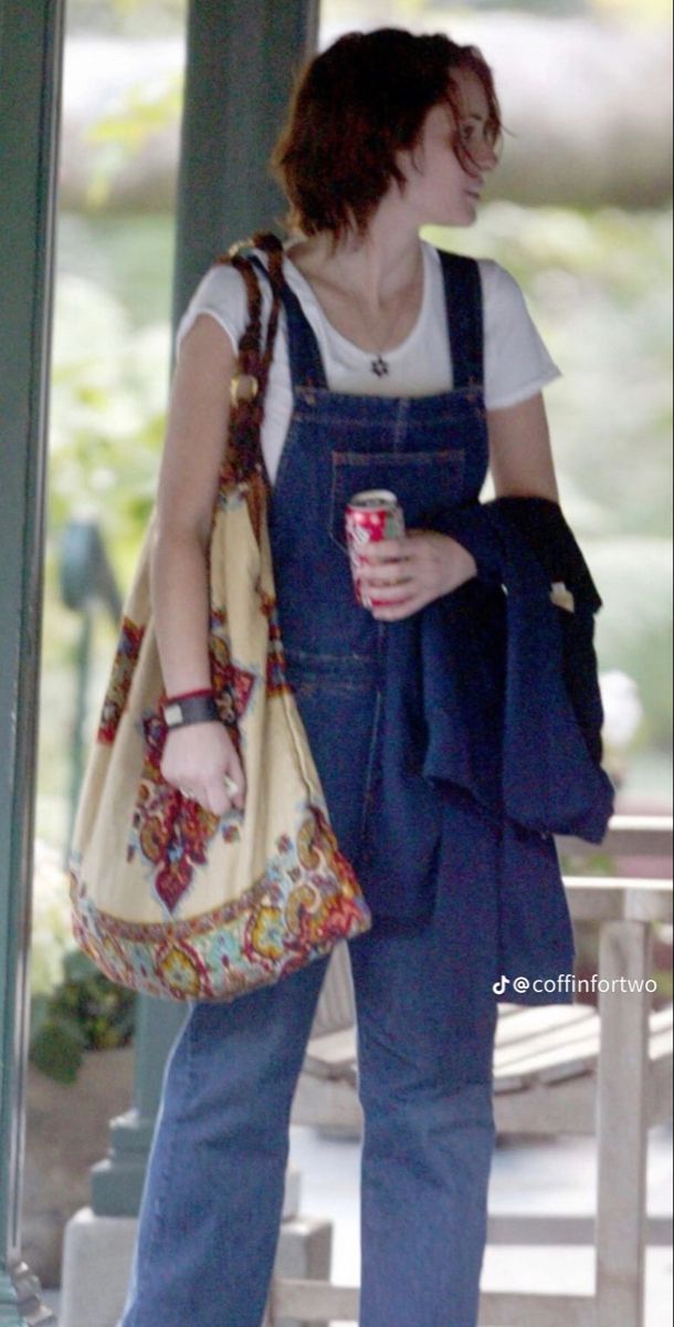 a woman in overalls holding a coffee cup