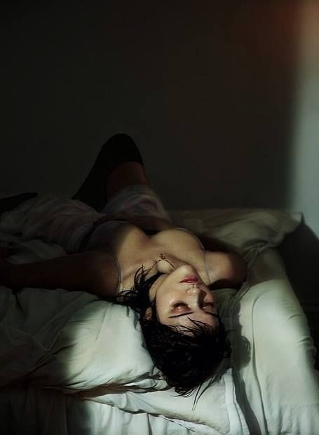 a man laying on top of a bed in the dark with his head down and eyes closed