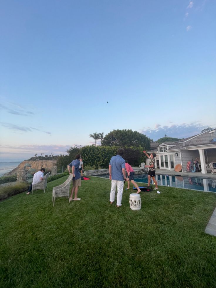 some people are playing badminton on the grass by the water in front of their house