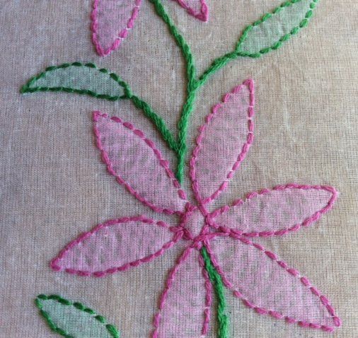 a pink flower with green leaves is embroidered onto a piece of cloth that has been stitched together