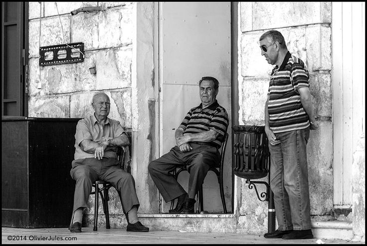 three men sitting on chairs in front of a building and one man standing next to the door