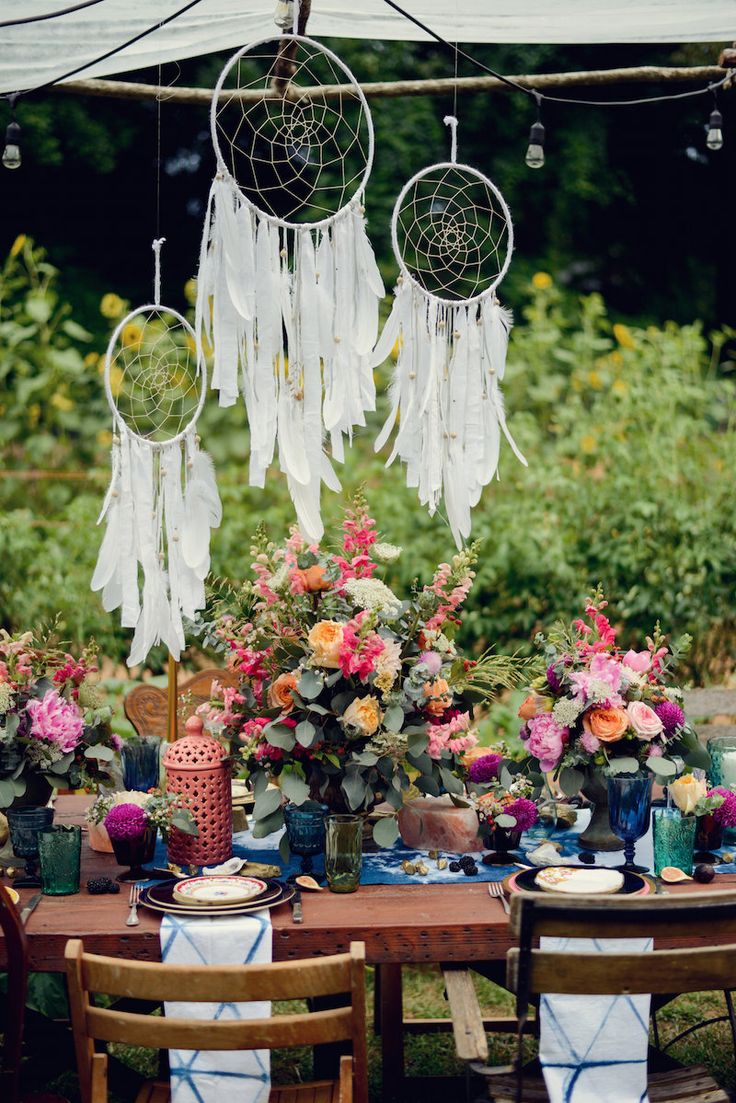 an outdoor table with flowers and dream catchers hanging from it