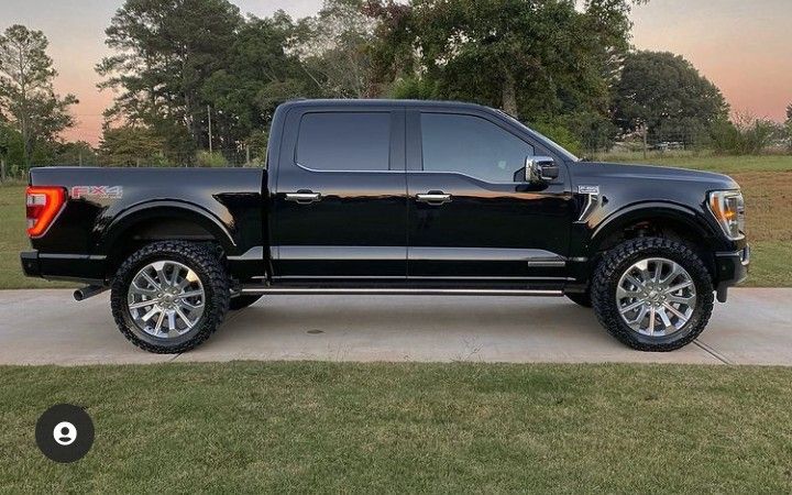 the black truck is parked on the driveway in front of some grass and trees,