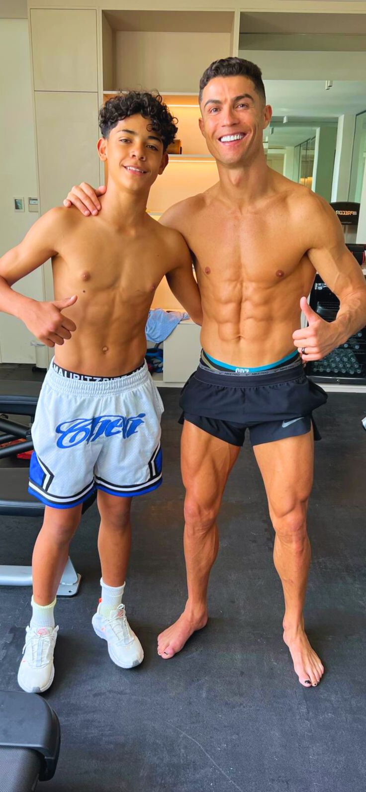 two men standing next to each other in front of a gym equipment area with one holding a water bottle