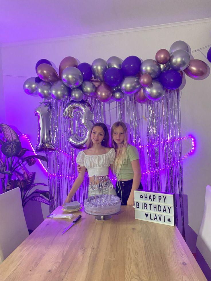 two girls standing in front of a table with a birthday cake and balloons on it