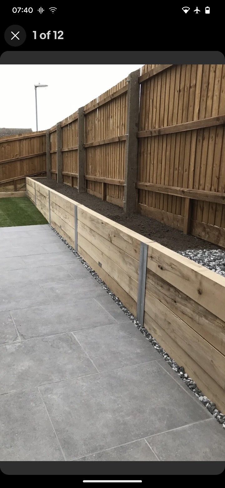 a wooden fence next to a grass covered yard with gravel on the ground and rocks in the middle