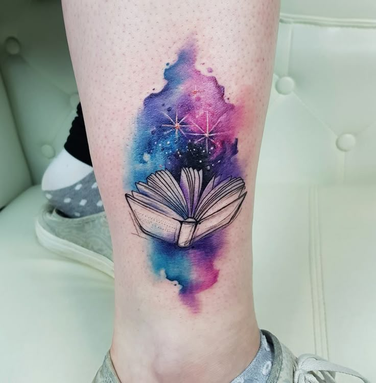 a woman's leg with an open book tattoo on her left thigh and stars in the sky above it