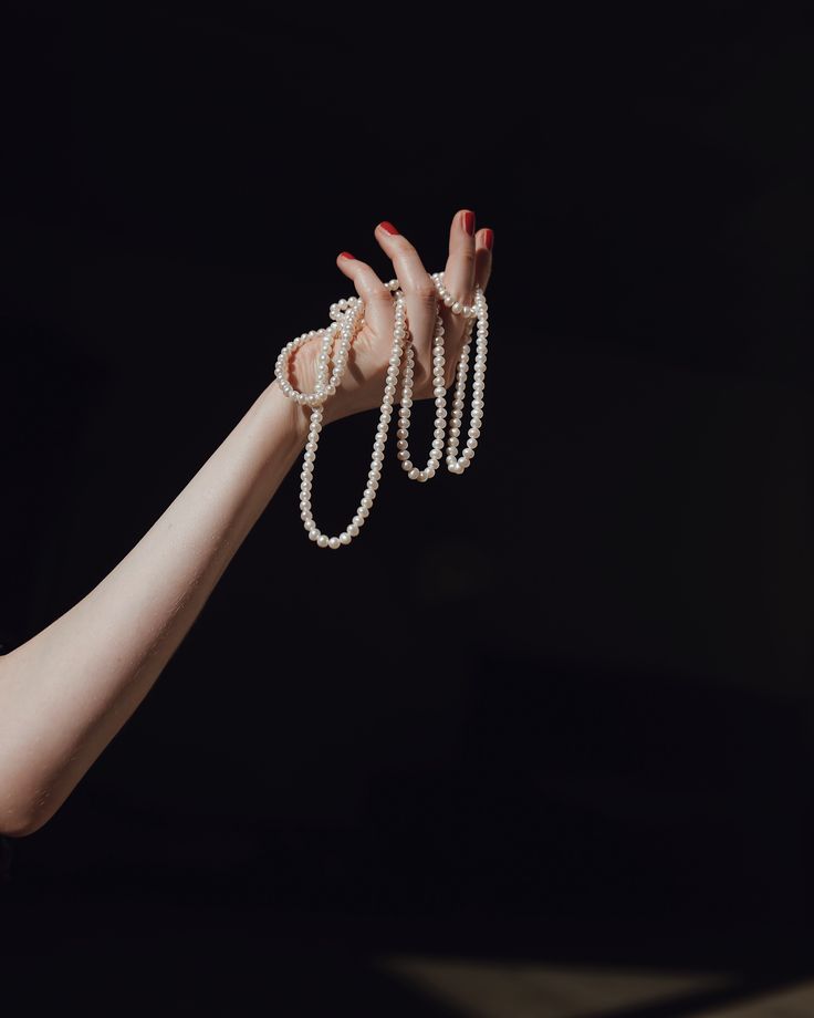 a woman's hand holding pearls in the air