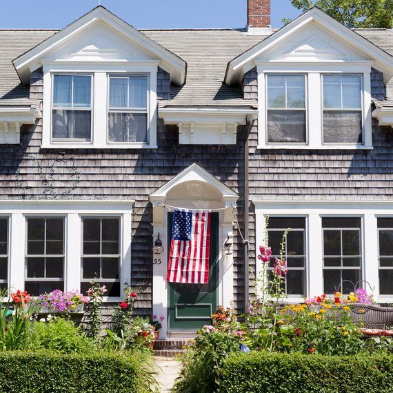 an american flag is hanging on the front door of a gray house with white trim