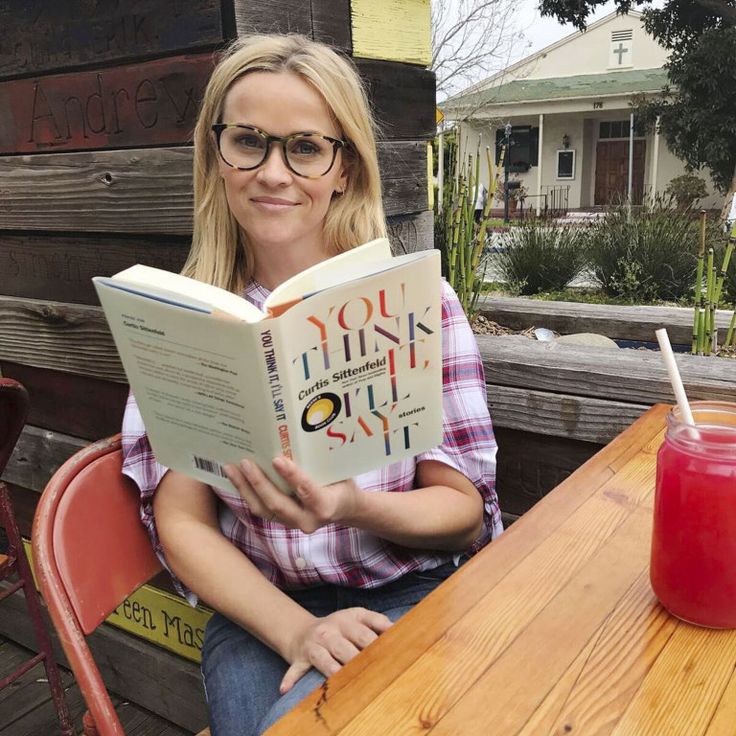 a woman sitting at a table with a book in front of her and a drink