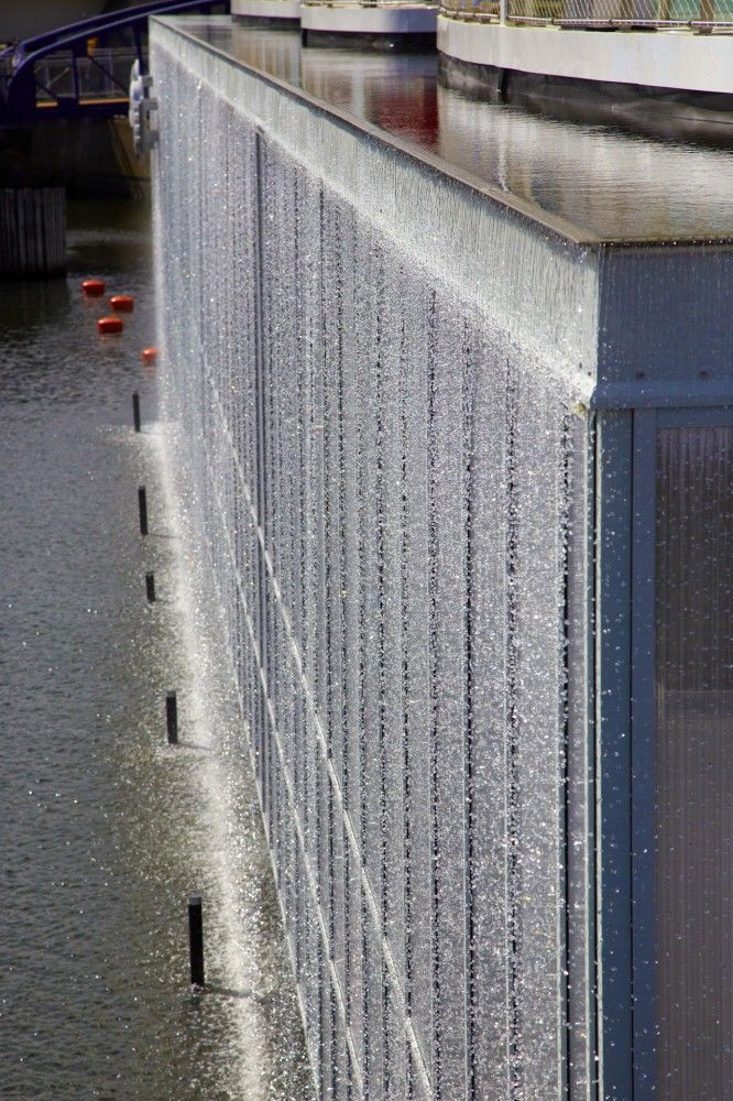 water spewing out from the side of a building next to a body of water