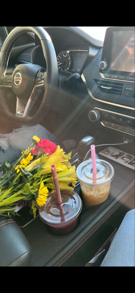 flowers and drinks sit on the dashboard of a car