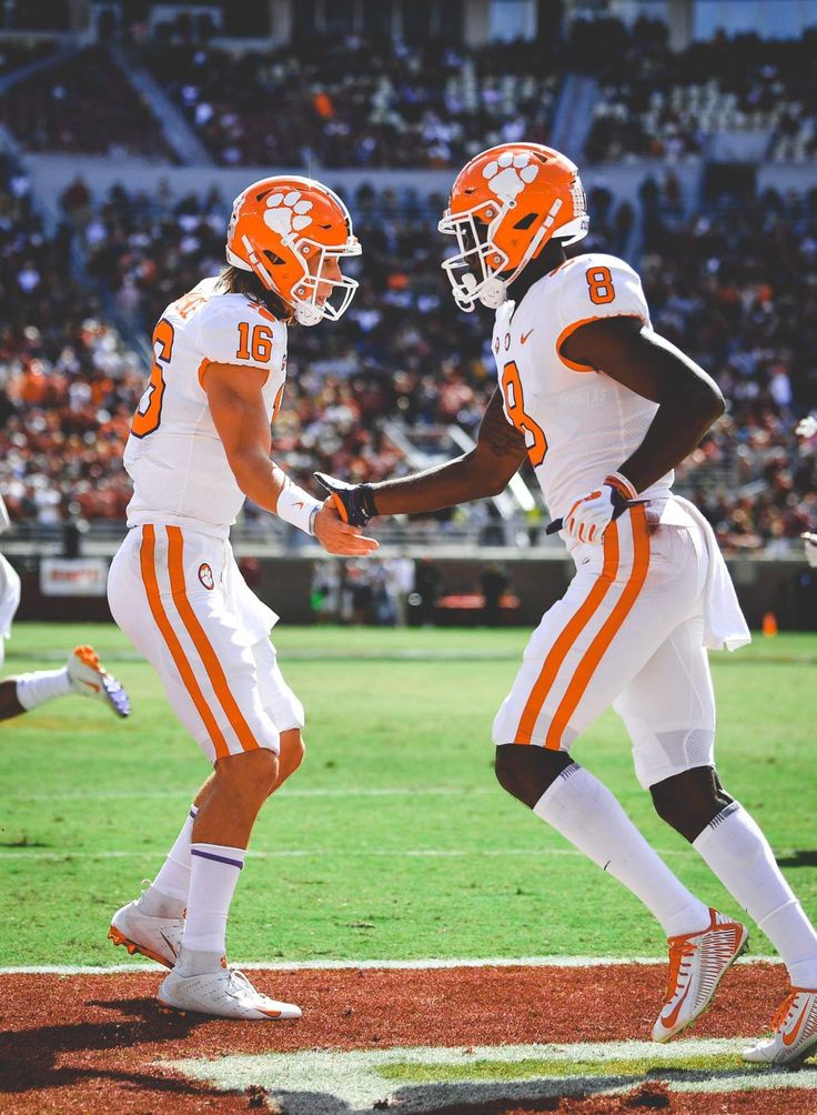 two football players in orange and white uniforms shaking hands on the field with an audience watching