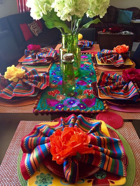 a colorful table setting with flowers in a vase and napkins on the placemats