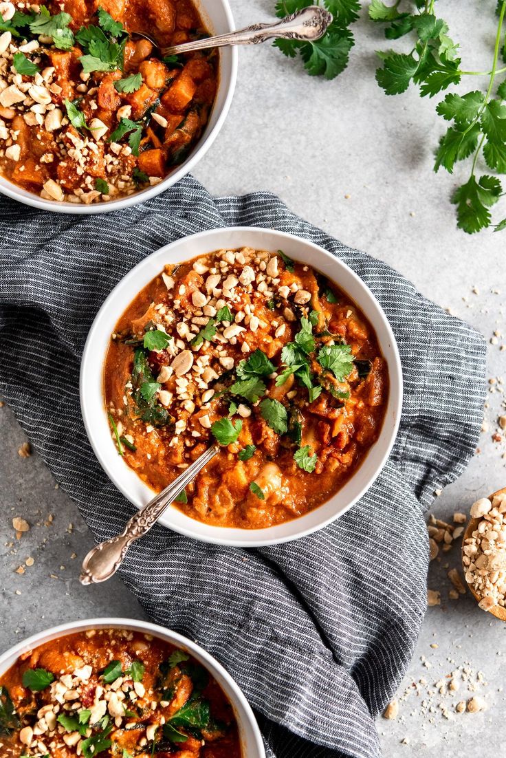 two white bowls filled with soup and garnished with cilantro, parsley and peanuts