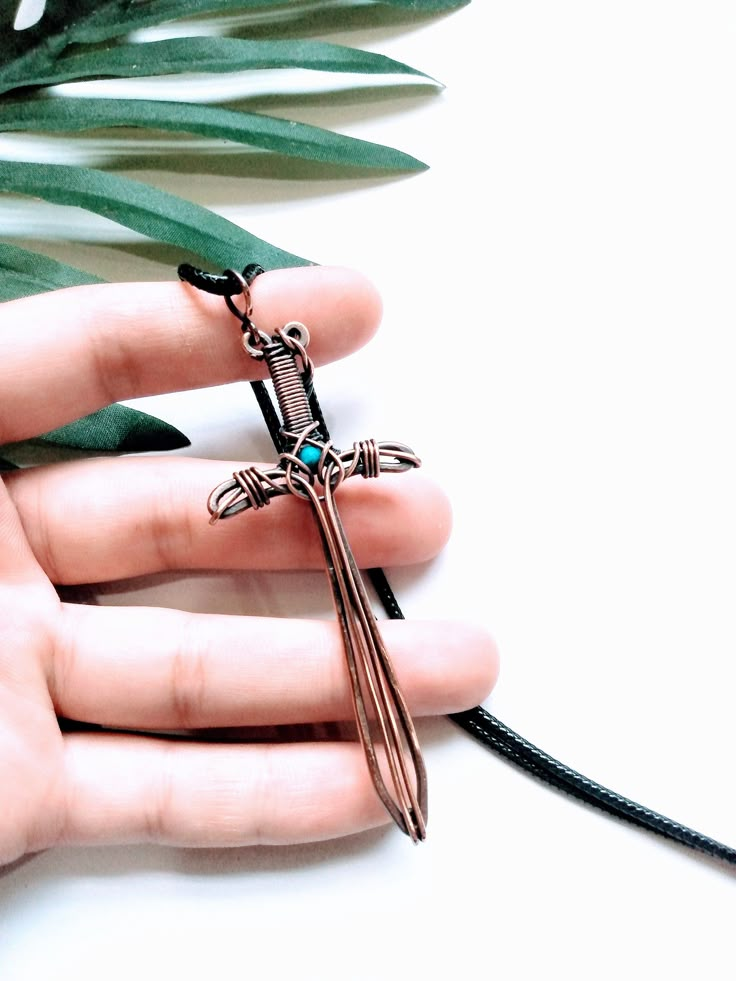 a person holding a cross pendant in their hand next to a plant with green leaves