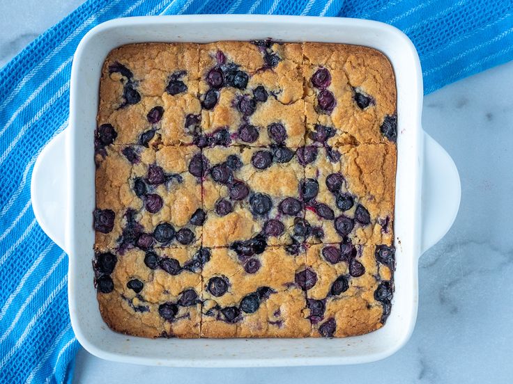 a blueberry cobbler in a white dish on a blue towel