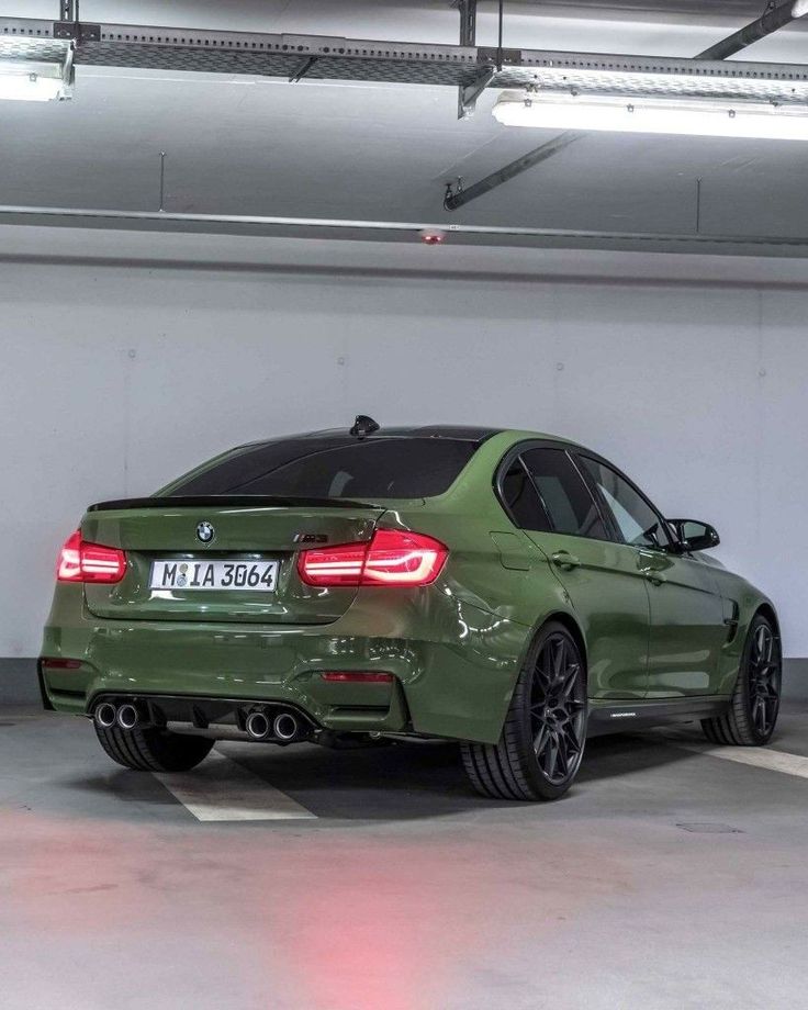 a green bmw car parked in a parking garage with its lights on and the back end showing