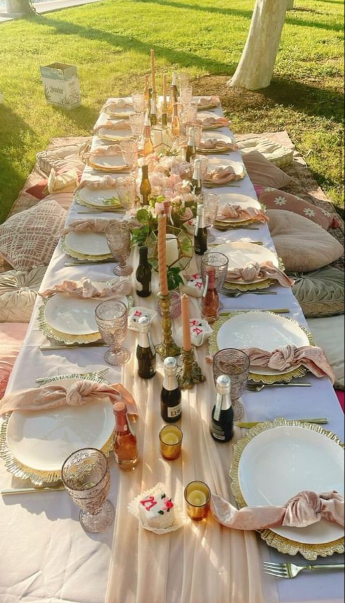 a long table with plates and candles on it in the middle of a park area