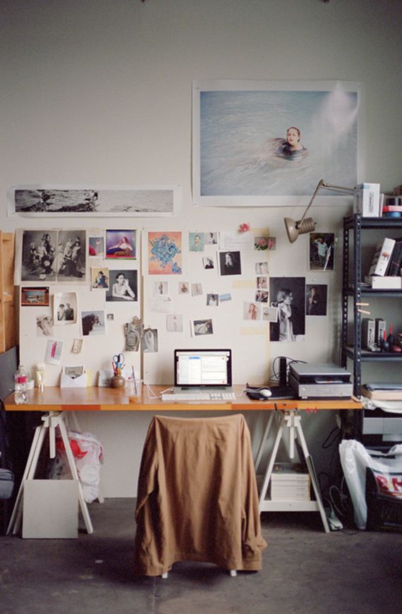 a desk with a laptop computer on top of it next to a wall covered in pictures