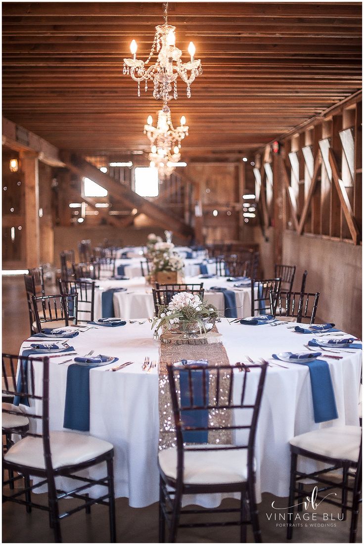 the tables are set with blue and white linens for an elegant wedding reception in a barn