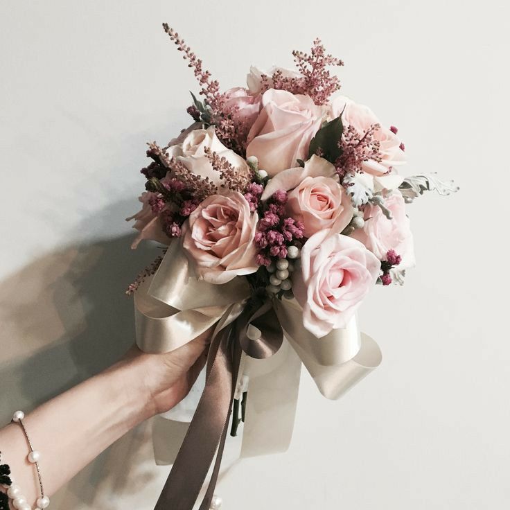 a woman's hand holding a bridal bouquet with pink roses and greenery