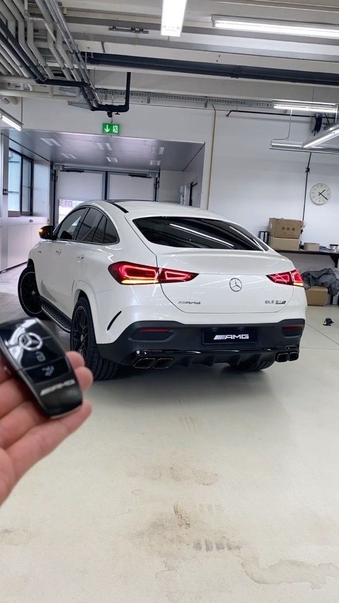 a hand holding a cell phone in front of a white car parked in a garage