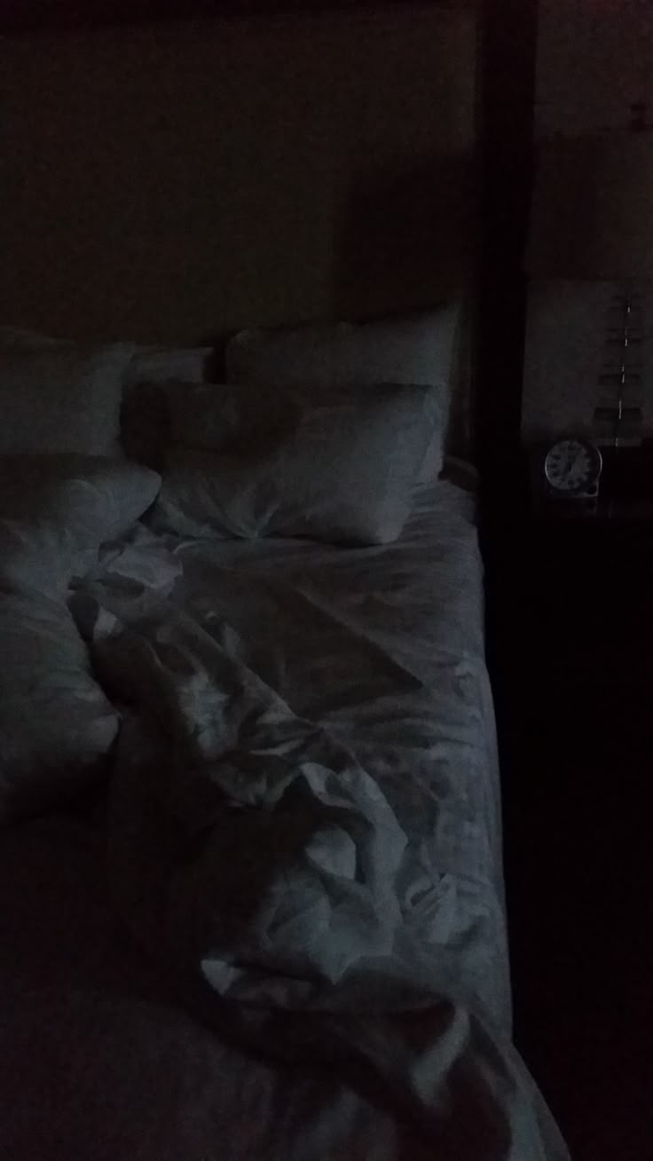 an unmade bed with white sheets and pillows in a dark room at night time