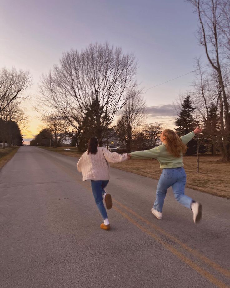 two girls running down the street in front of trees and grass, one is holding her arms out