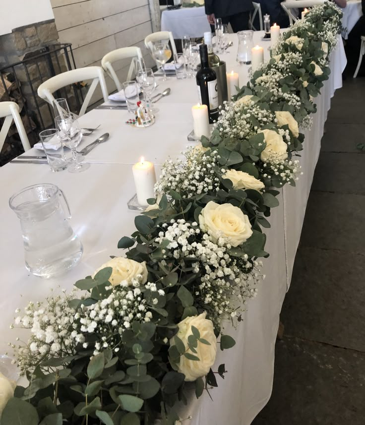 a long table with white flowers and greenery on it, along with wine glasses