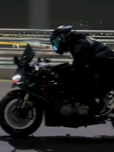 a man riding on the back of a motorcycle down a street next to a bridge