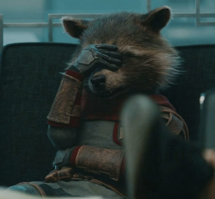 a raccoon is sitting in an office chair with his head on the arm of someone's hand