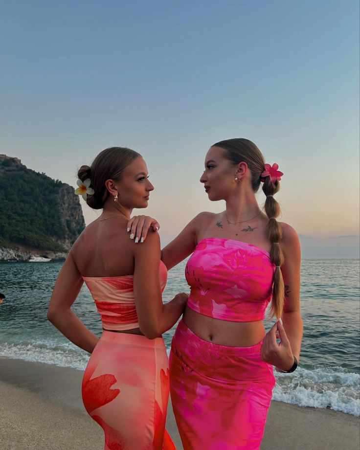 two beautiful women standing next to each other on a beach