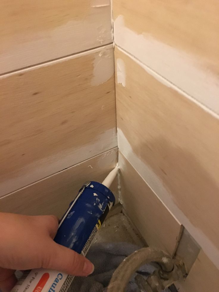 a person spray painting the wall in a bathroom with wood paneling and white paint