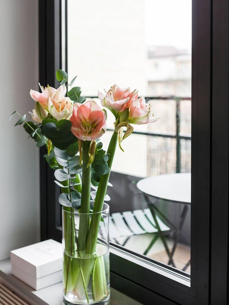 three pink flowers in a vase on a window sill next to a white table