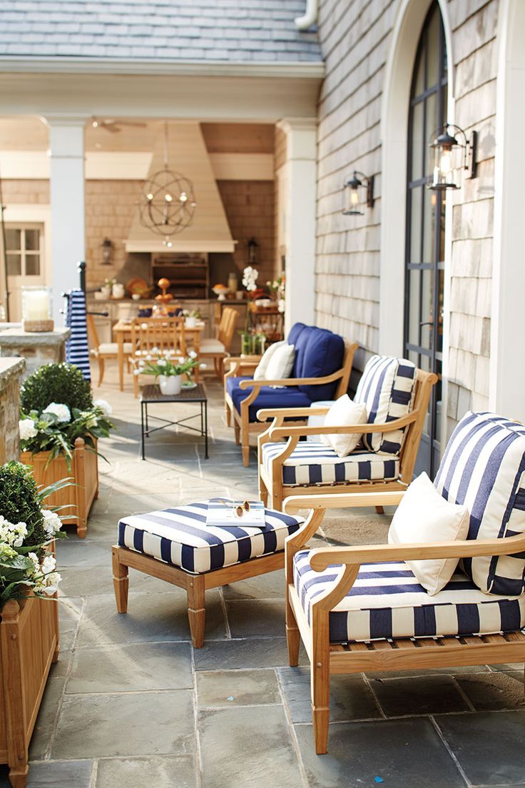 the front porch is decorated with blue and white striped chairs, potted plants, and outdoor furniture