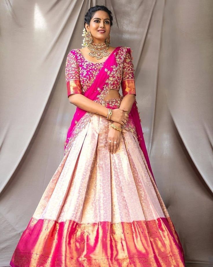 a woman in a pink and gold lehenga standing next to a gray backdrop