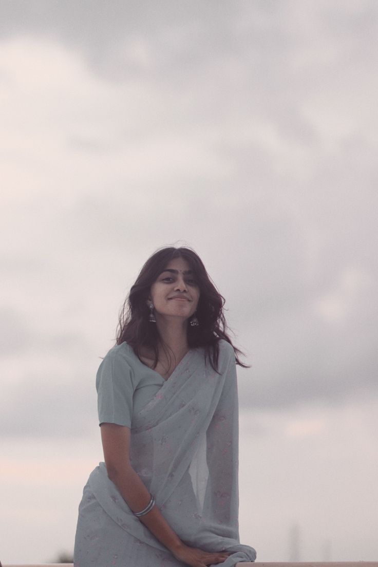 a woman sitting on top of a wooden bench next to the ocean with her eyes closed