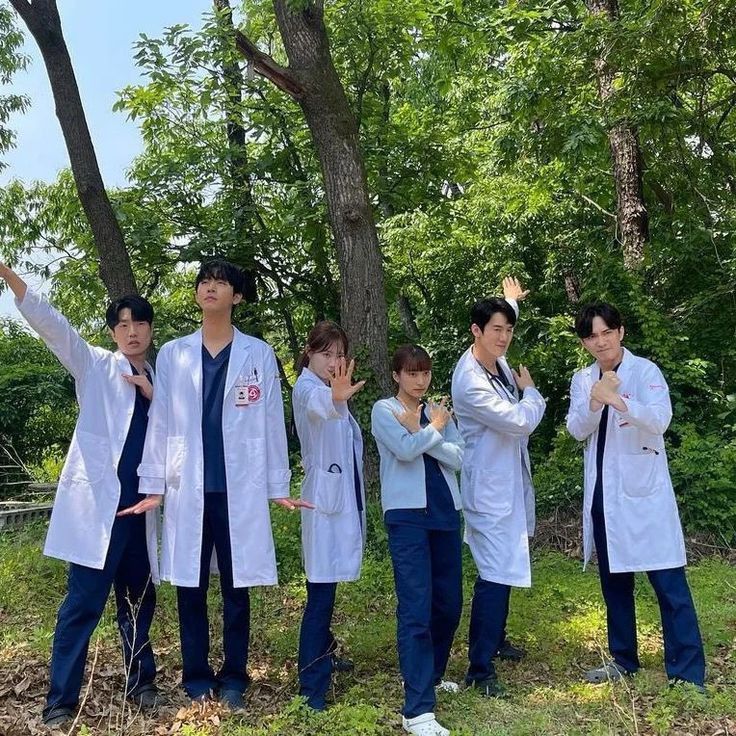 four young men in lab coats standing next to each other on the grass and trees