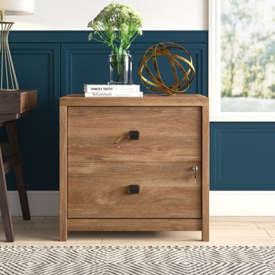 a wooden cabinet with two drawers in front of a blue wall and a lamp on the side table