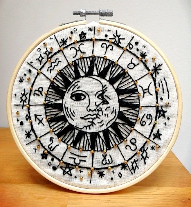 an embroidered sun and moon with zodiac signs on the front is sitting on top of a wooden table