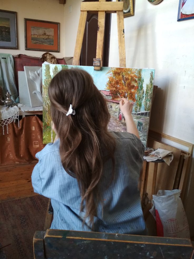 a woman sitting in front of an easel painting