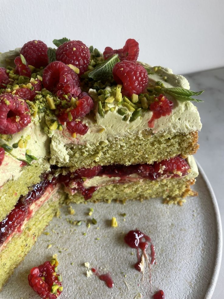 a cake with raspberries and pistachio on top is cut in half