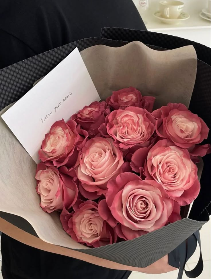 a woman holding a bouquet of pink roses with a note attached to the top of it