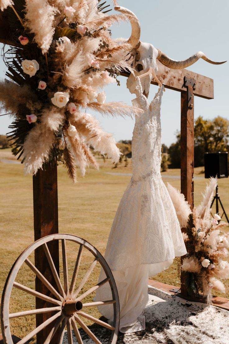 a wedding dress hanging on a wooden pole with flowers and feathers in front of it