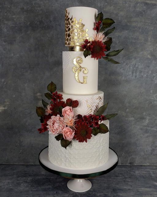 a three tiered wedding cake with red flowers and gold numbers on the top layer