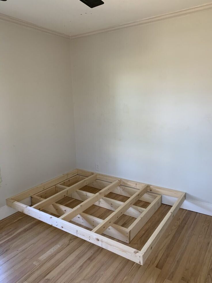 an unfinished bed frame in the middle of a room with hard wood flooring and white walls