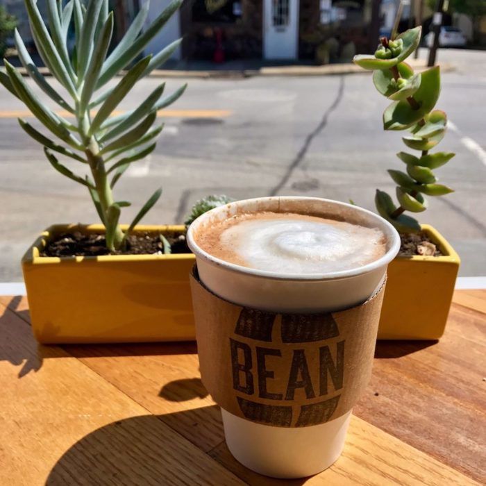 a cup of coffee sitting on top of a wooden table next to a potted plant