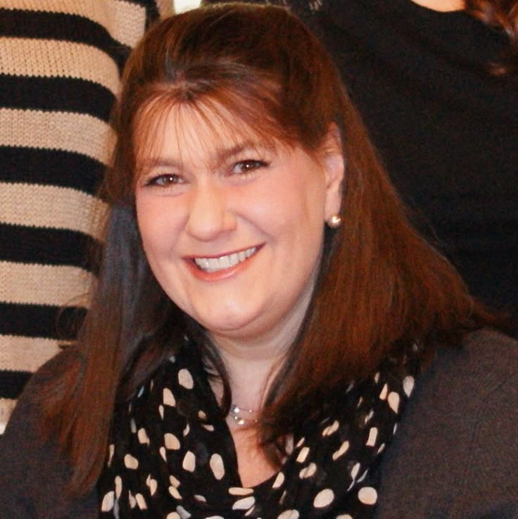 a woman with long hair smiling and wearing a black and white polka dot scarf around her neck