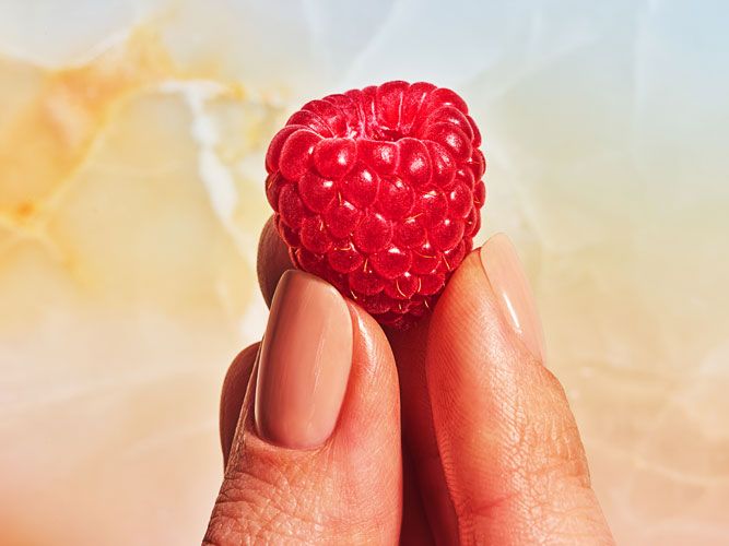 a woman's hand holding a raspberry in the shape of a heart